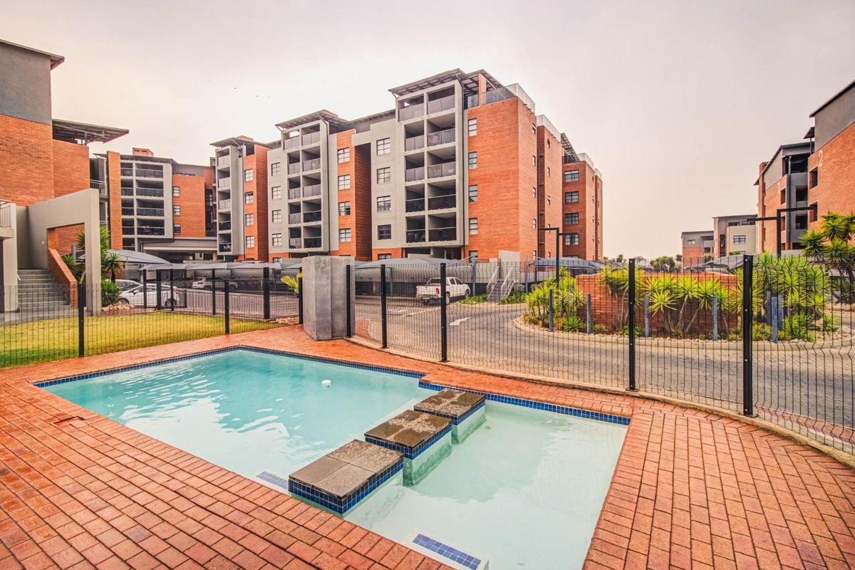 A well-maintained communal swimming pool area featuring brick paving and secure mesh fencing, set within a modern townhouse complex.