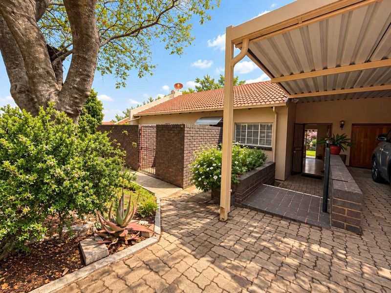 Front exterior view featuring a paved driveway, covered carport, brick boundary wall, and established garden area.
