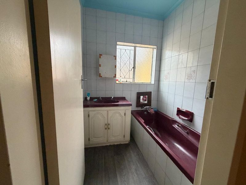 A compact bathroom featuring a built-in vanity, bathtub, and tiled walls, offering a functional space ready for modern updates and renovation.