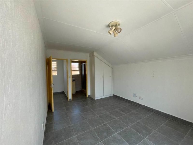 An empty bedroom featuring tiled flooring, a sloped ceiling, and built-in cupboards, with an adjoining en-suite bathroom.
