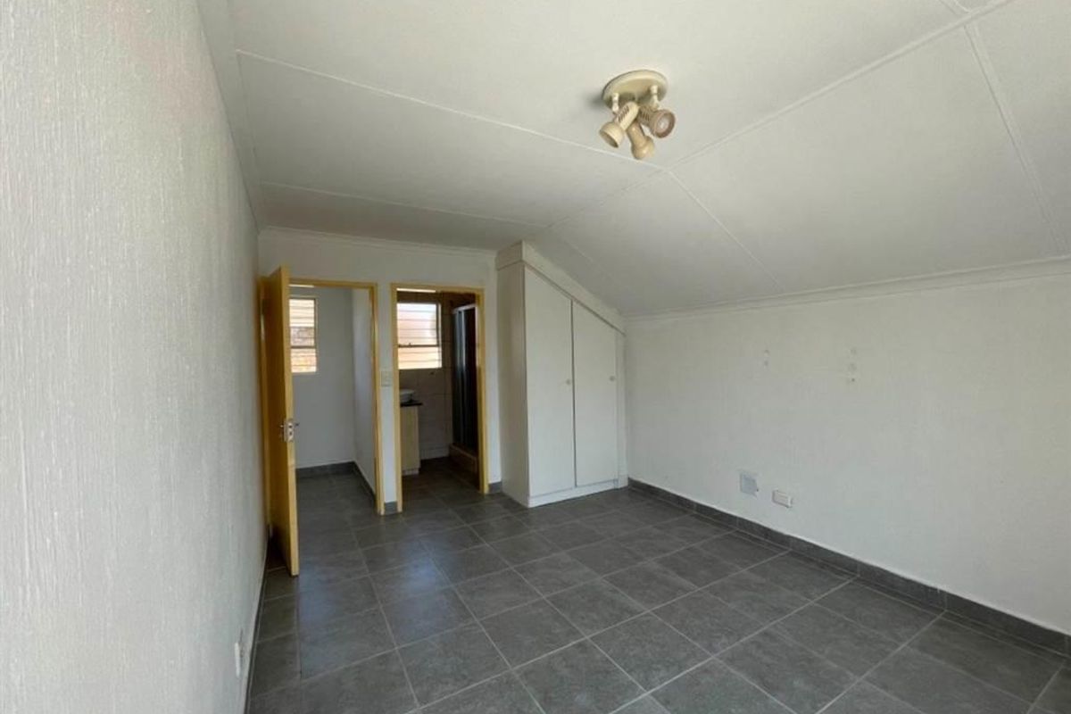 An empty bedroom featuring tiled flooring, a sloped ceiling, and built-in cupboards, with an adjoining en-suite bathroom.