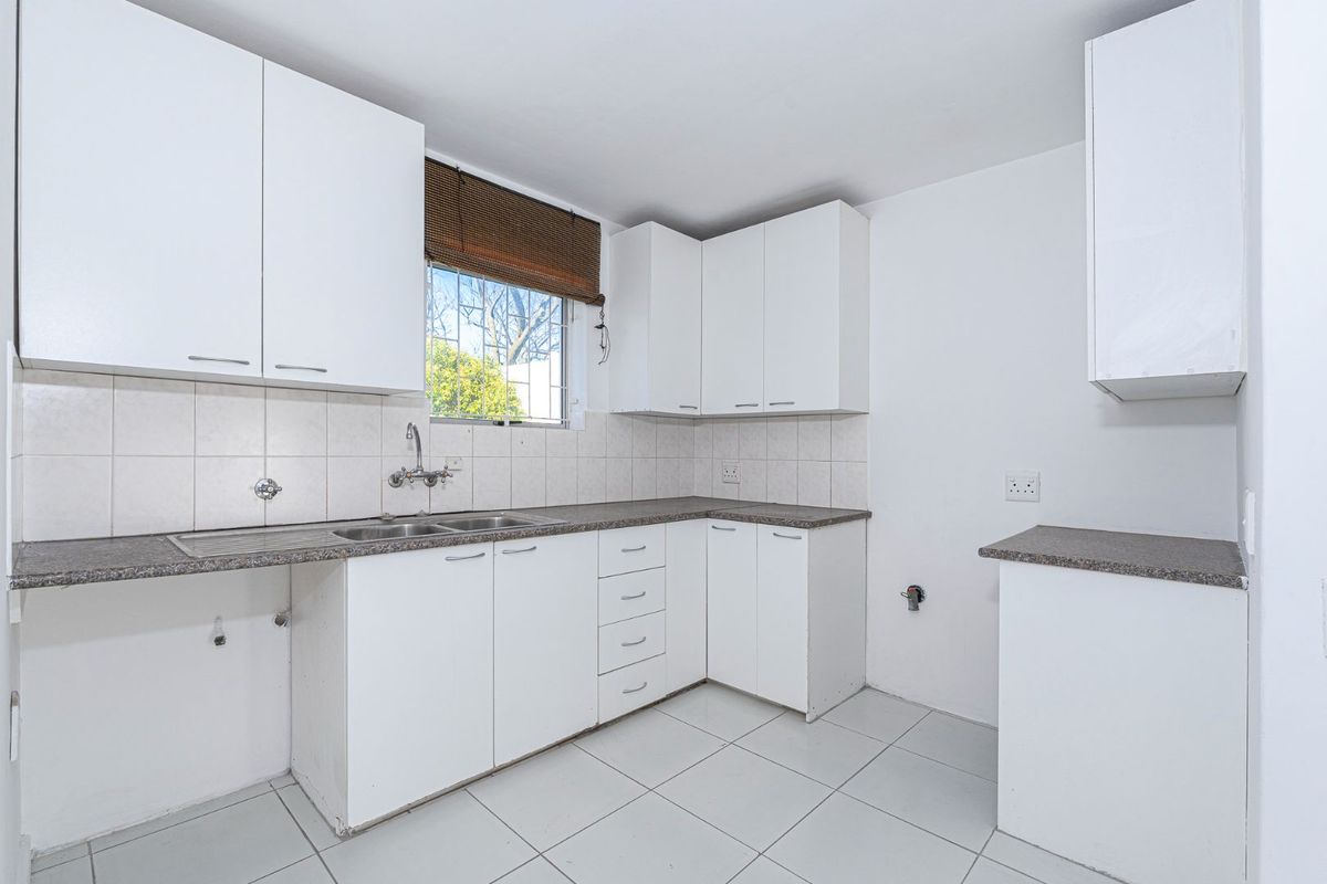 A functional kitchen featuring white cabinetry, granite-look countertops, a double stainless steel sink, and tiled flooring, ready for customization.