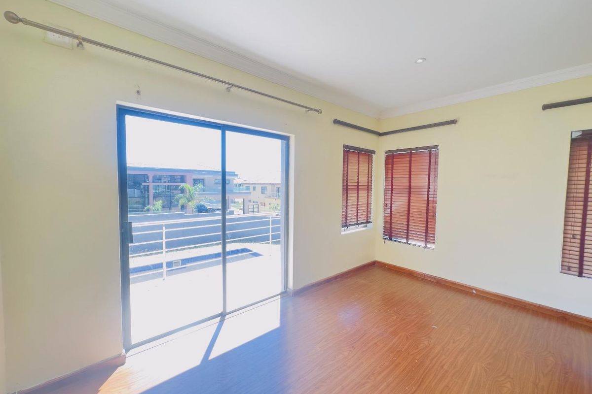 Bright bedroom featuring laminate flooring, sliding glass doors leading to a balcony, and fitted wooden venetian blinds.