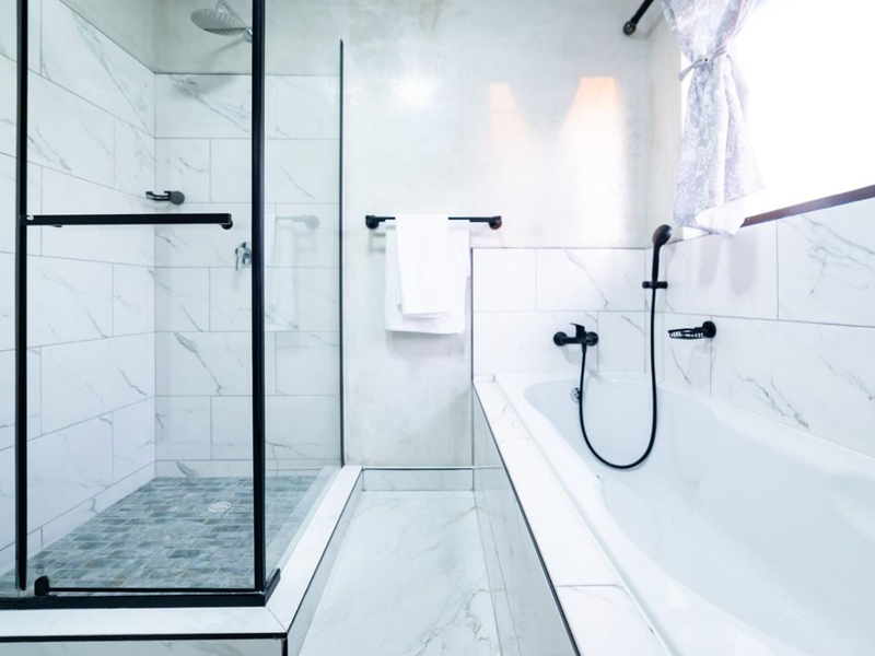 Modern bathroom featuring a walk-in shower with glass enclosure, a separate bathtub, and contemporary black matte fixtures with marble-look tiling.