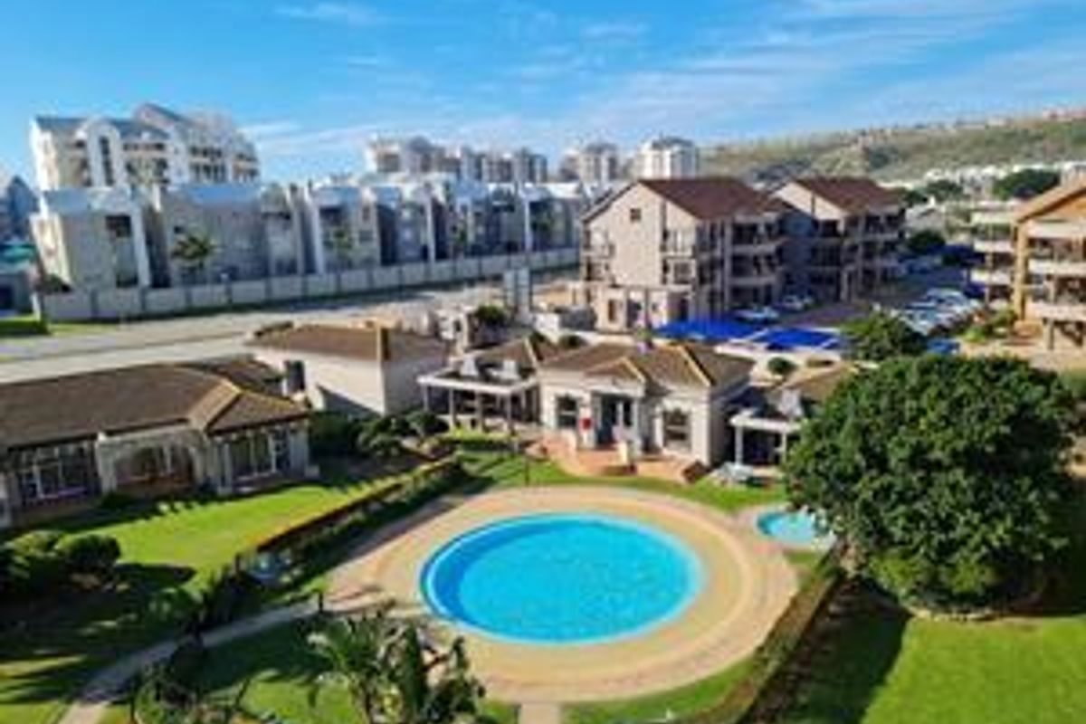 Aerial view of a residential apartment complex featuring a central swimming pool, landscaped gardens, and communal clubhouse facilities.