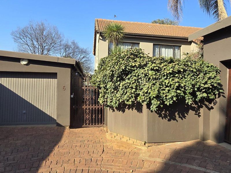 Front exterior view of the townhouse featuring a paved driveway, garage access, and a secure gated entrance with established landscaping.