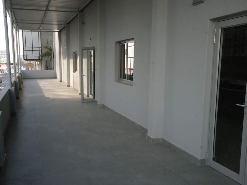 A spacious, covered balcony featuring tiled flooring and modern aluminium-framed glass doors, providing access to the interior office or commercial space.
