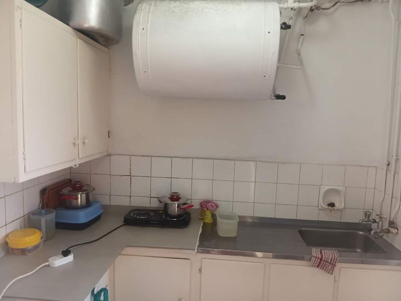 A compact kitchen featuring basic cabinetry, a stainless steel sink, tiled backsplash, and a wall-mounted electric water heater.