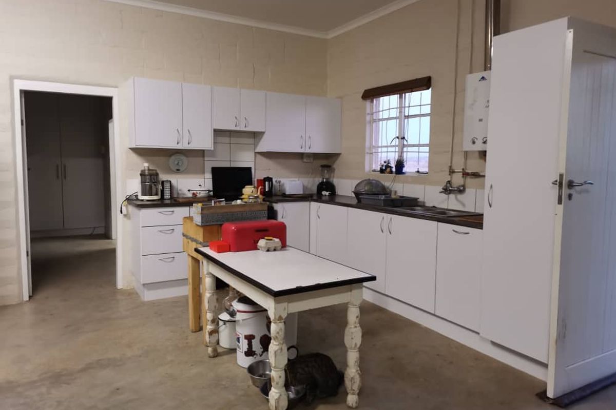 Functional kitchen area featuring white cabinetry, laminate countertops, a stainless steel sink, and a wall-mounted gas geyser.