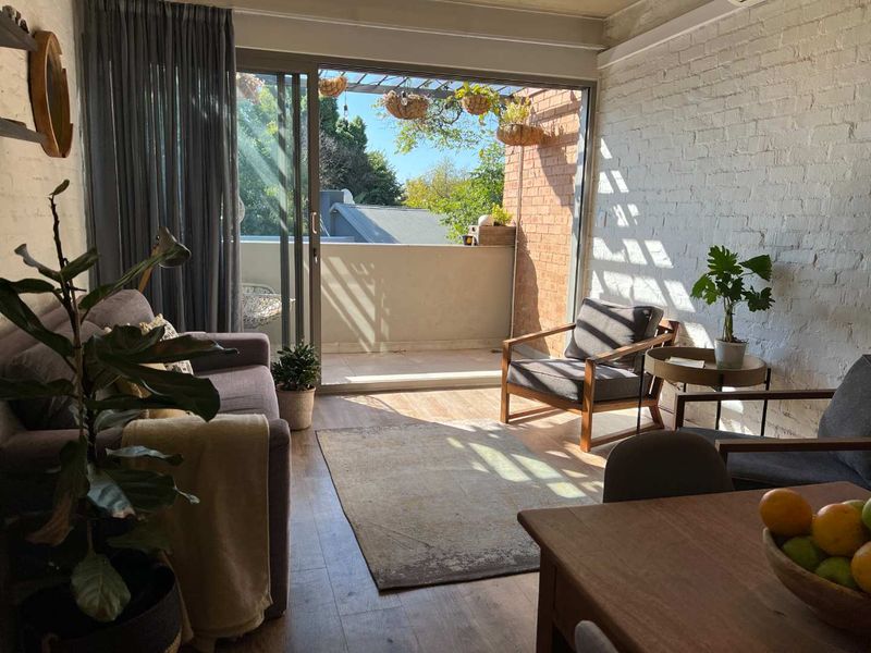 Bright living room featuring exposed white brick walls, laminate flooring, and large sliding glass doors providing direct access to a private balcony.