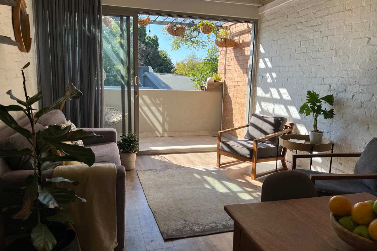 Bright living room featuring exposed white brick walls, laminate flooring, and large sliding glass doors providing direct access to a private balcony.