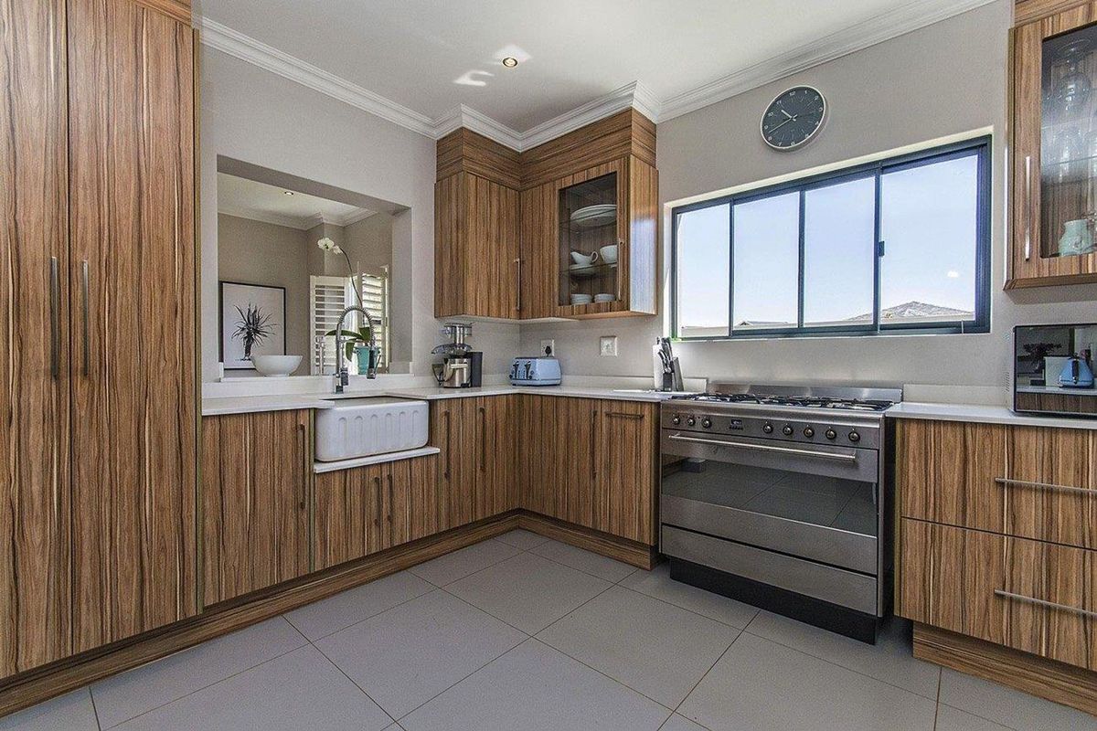 Modern kitchen featuring wood-grain cabinetry, white countertops, a farmhouse-style sink, and a stainless steel gas range with an integrated extractor.