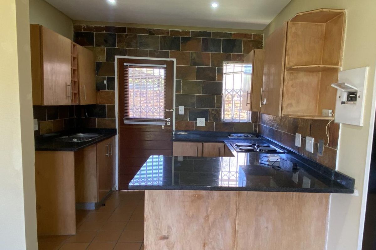 A functional kitchen featuring granite countertops, built-in cabinetry, and a slate tile backsplash, requiring some finishing touches to complete the space.