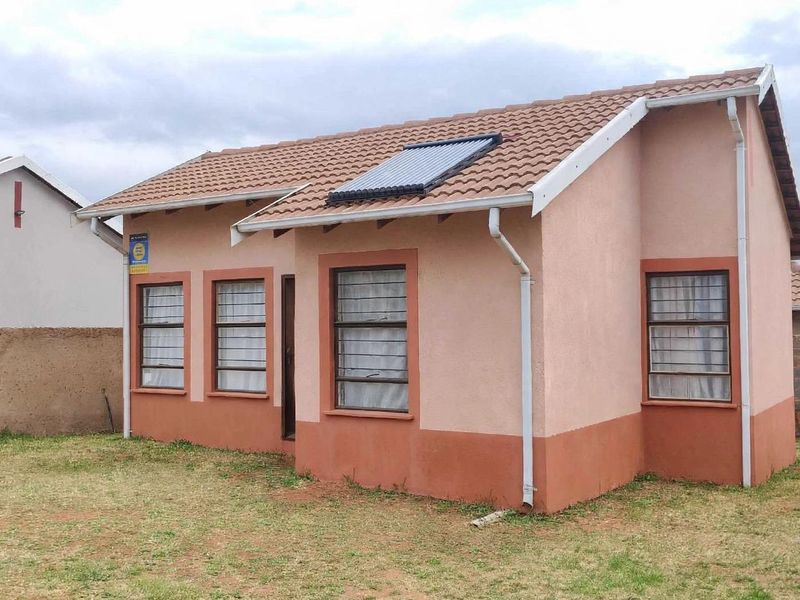 Rear view of a detached house featuring a tiled roof with a solar water heater, painted exterior walls, and security-barred windows.