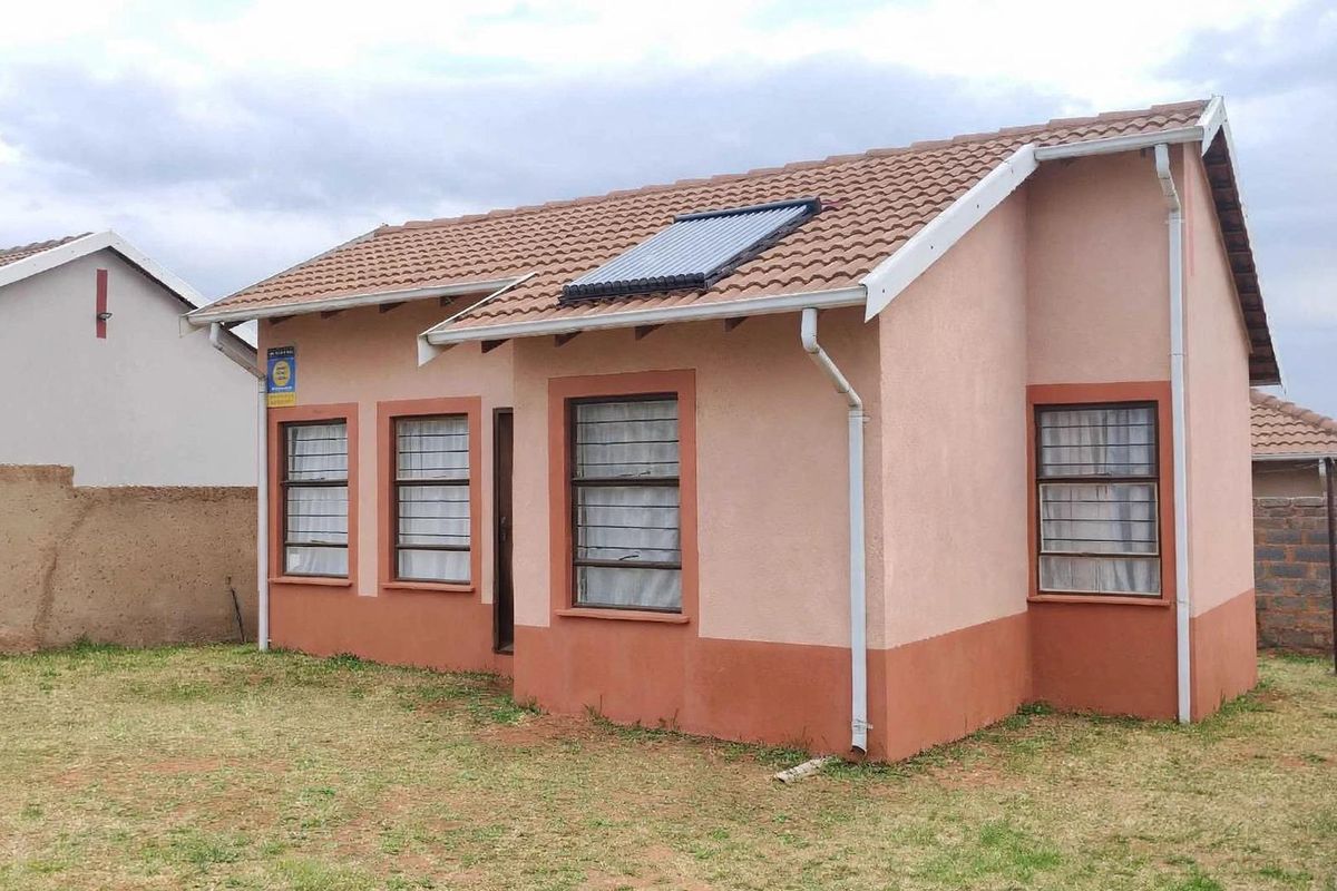 Rear view of a detached house featuring a tiled roof with a solar water heater, painted exterior walls, and security-barred windows.