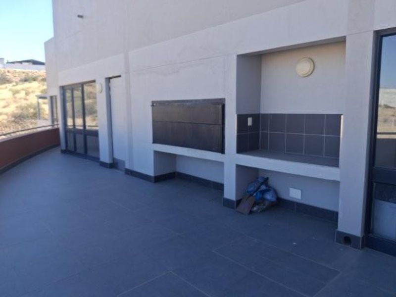 Spacious covered balcony featuring a built-in braai, tiled flooring, and recessed wall lighting, offering a functional outdoor entertainment area.
