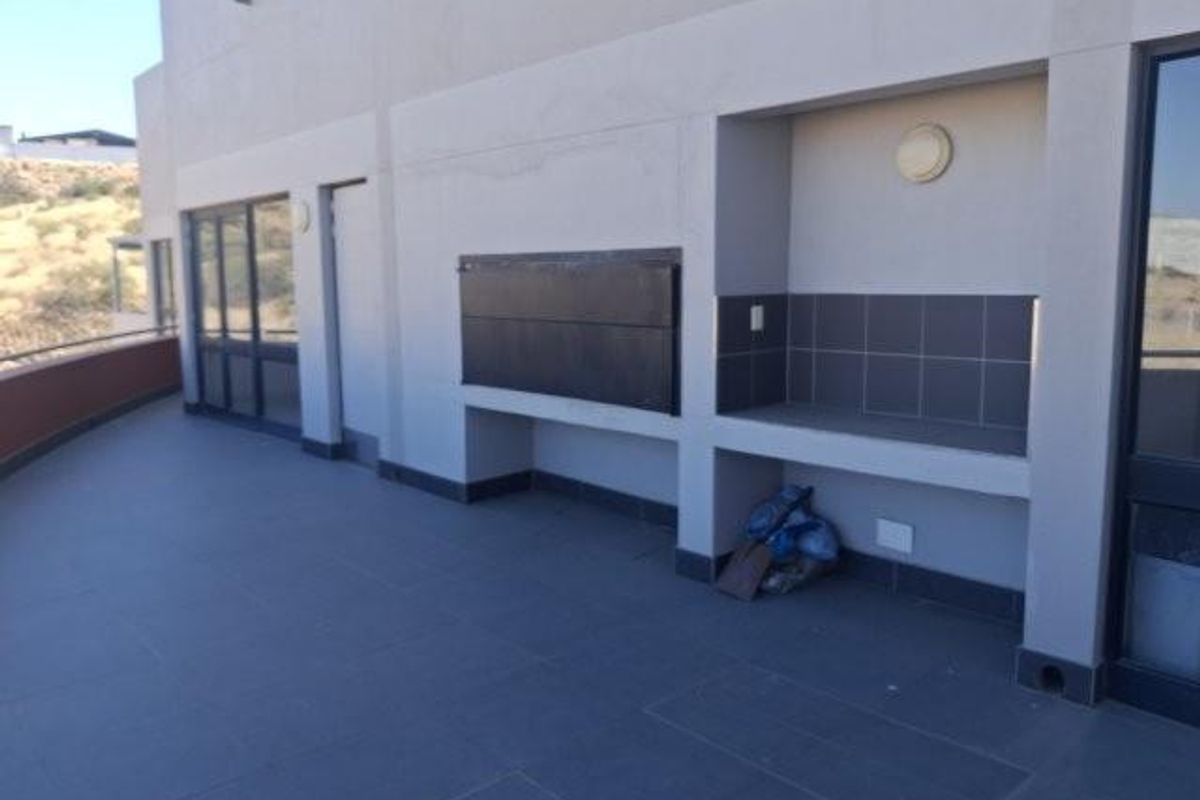 Spacious covered balcony featuring a built-in braai, tiled flooring, and recessed wall lighting, offering a functional outdoor entertainment area.