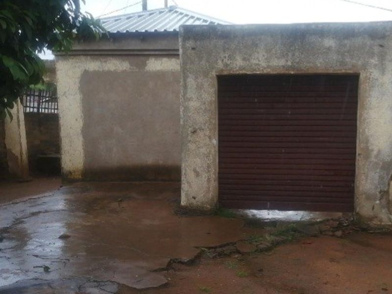 A detached garage structure featuring a roller shutter door and a weathered exterior, situated on a concrete driveway with visible surface cracking.