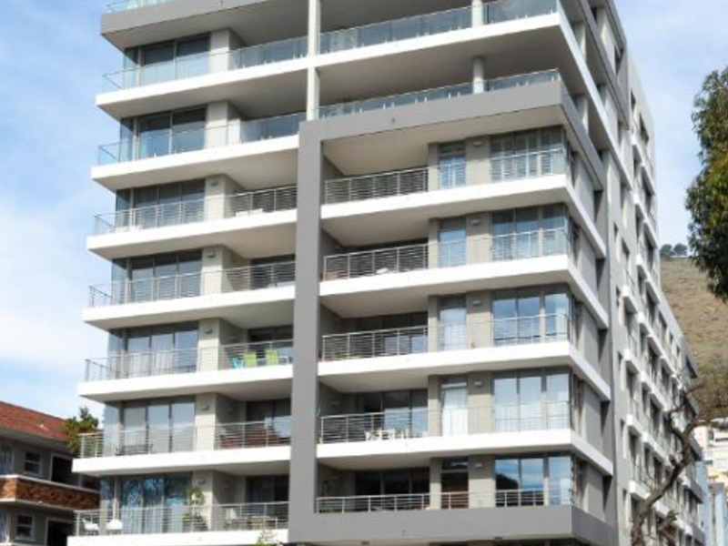 Modern multi-story apartment building featuring glass balconies, stone facade detailing, and a secure ground-level parking entrance.