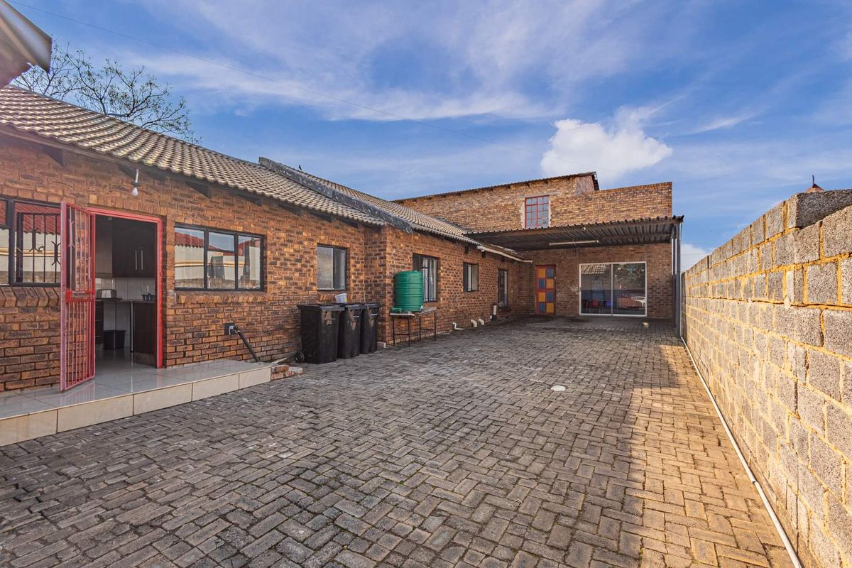 A spacious rear exterior area featuring a paved courtyard, face brick building facade, and a covered carport structure.
