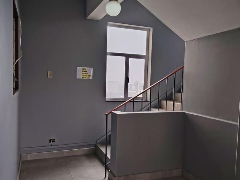 A clean, modern hallway featuring tiled flooring, a staircase with a metal handrail, and neutral grey wall finishes.