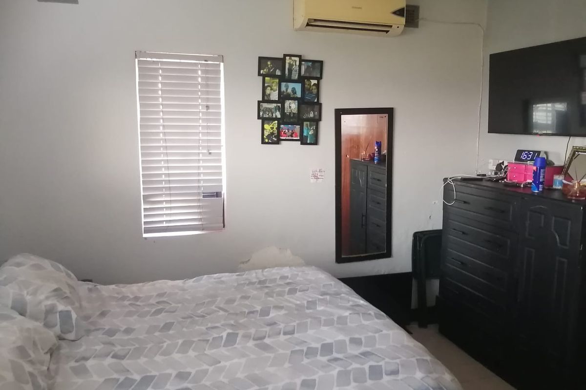 A bedroom featuring an air conditioning unit, venetian blinds, and a ventilation grille. The room shows signs of wear on the wall finish.