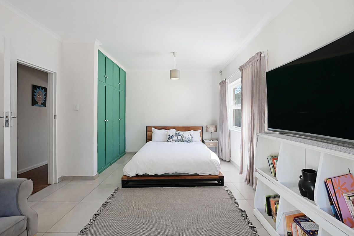 A bright bedroom featuring built-in green cabinetry, tiled flooring, and large windows allowing for natural light.