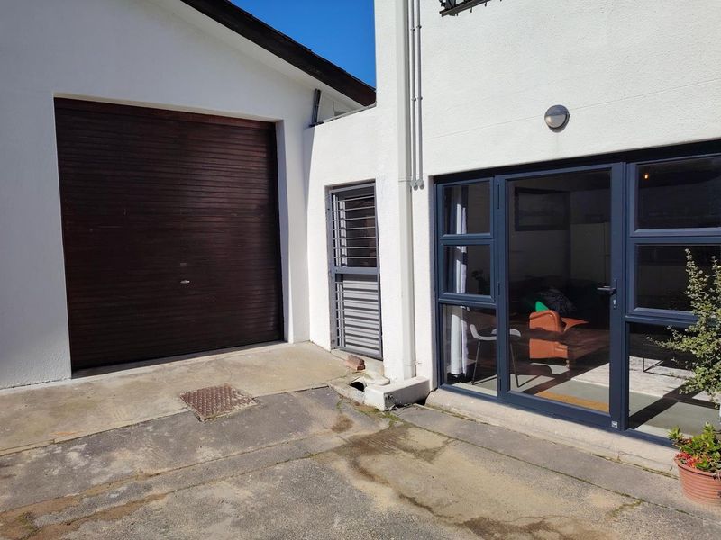 Rear exterior view of the cottage featuring a garage door, security gate, and modern aluminium sliding doors leading into the living area.