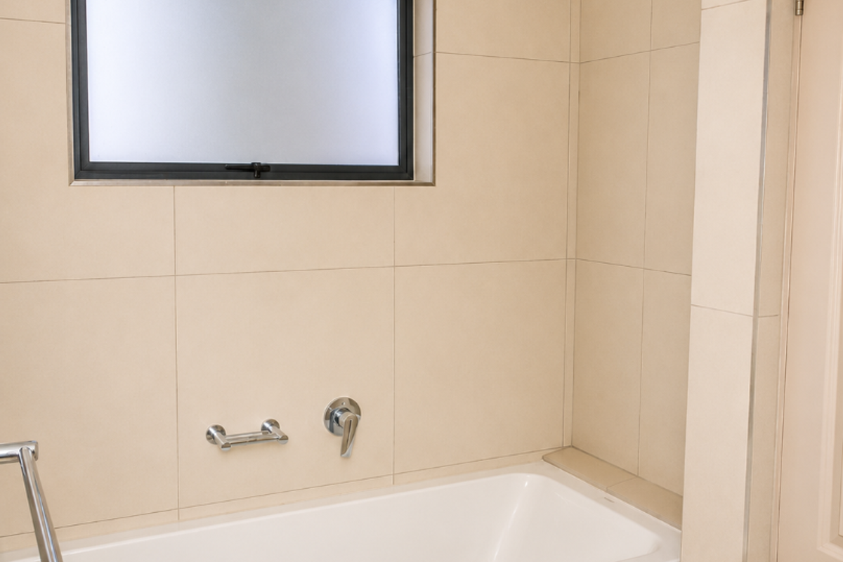 A clean, modern bathroom featuring a built-in bathtub with chrome mixer tap, tiled walls, and a frosted window for privacy.