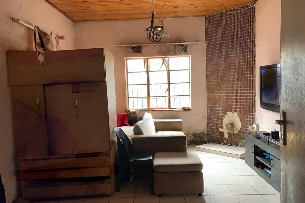 A living room featuring a timber-clad ceiling, tiled flooring, and a tiled fireplace surround, requiring significant cosmetic renovation and wall repairs.