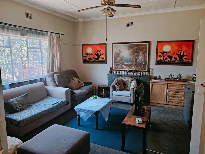A traditional living room featuring a fireplace, ceiling fan, and large windows with security bars, offering a comfortable and functional living space.