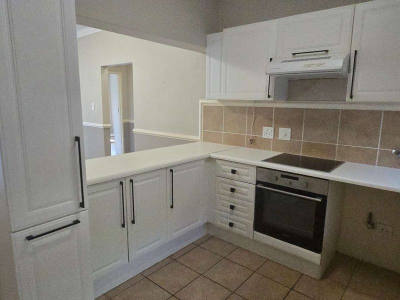 A clean, functional kitchen featuring white cabinetry, built-in oven and hob, tiled backsplash, and a convenient pass-through window overlooking the living area.