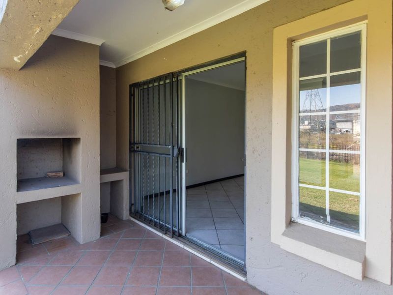 Covered patio featuring a built-in braai, tiled flooring, and a security gate leading into the apartment interior.
