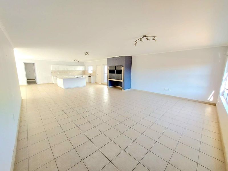 Spacious open-plan living area featuring a modern kitchen with island, tiled flooring throughout, and a prominent built-in fireplace, offering a versatile layout.