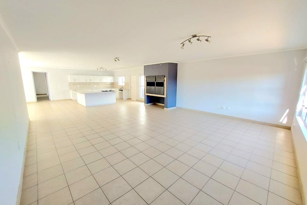 Spacious open-plan living area featuring a modern kitchen with island, tiled flooring throughout, and a prominent built-in fireplace, offering a versatile layout.