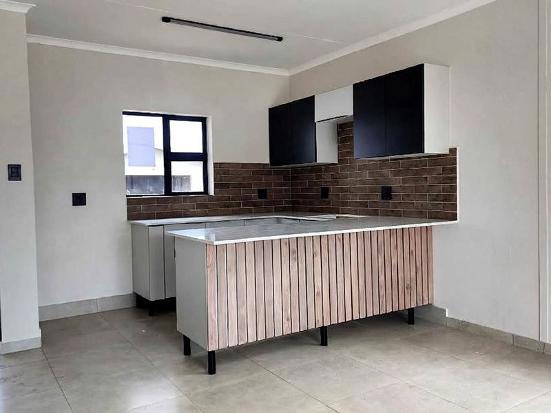 A modern, empty kitchen featuring sleek black and wood-panelled cabinetry, stone countertops, and a decorative tiled backsplash with neutral floor tiles.