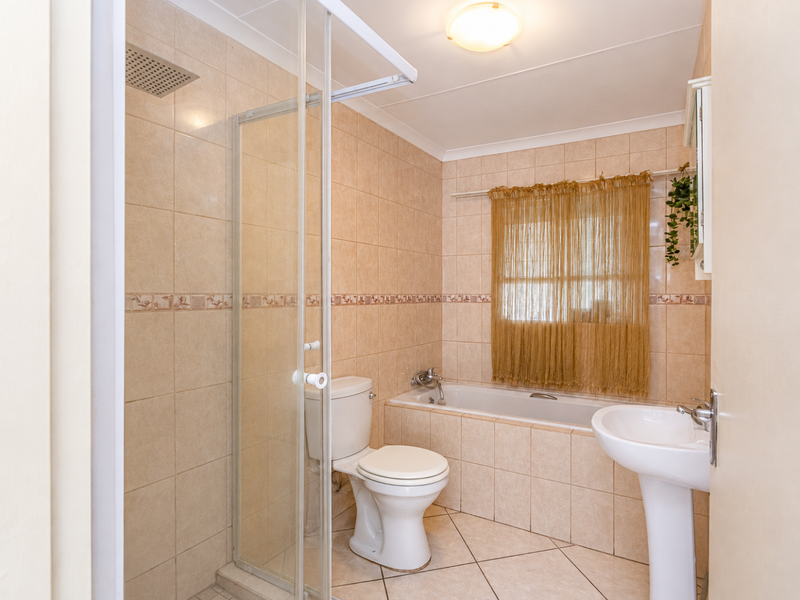 A functional bathroom featuring a separate shower enclosure, built-in bathtub, pedestal basin, and neutral ceramic tiling throughout.