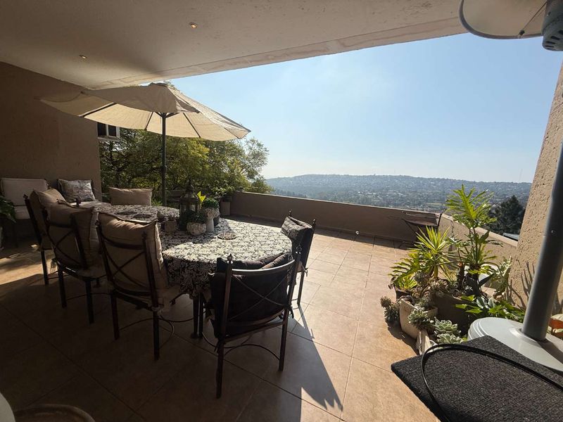 A spacious covered balcony featuring tiled flooring and recessed lighting, offering expansive elevated views of the surrounding landscape.