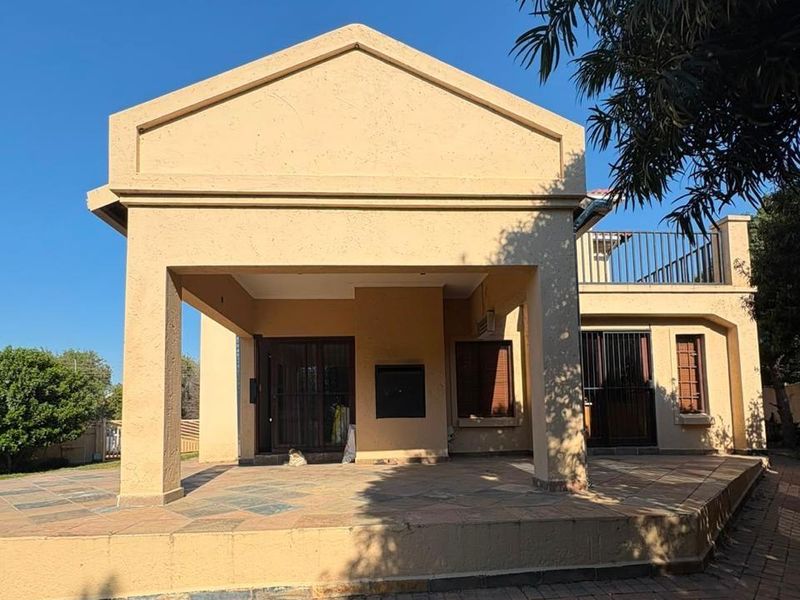 Rear view of the house featuring a covered patio area with stone tiling, security gates, and an upper-level balcony.