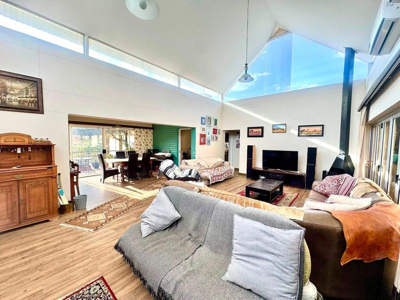 Spacious open-plan living area featuring a dramatic vaulted ceiling, clerestory windows for natural light, a wood-burning fireplace, and direct access to the outdoor patio.