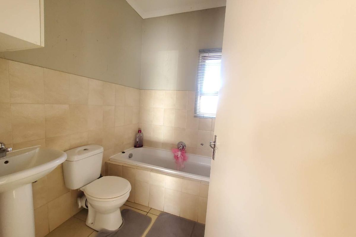 A functional bathroom featuring a pedestal basin, a standard toilet, and a tiled bathtub with a window.
