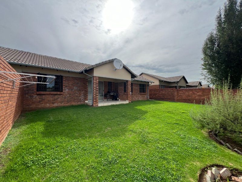 Rear view of the townhouse featuring a face brick facade, covered patio, and a private garden enclosed by brick boundary walls.