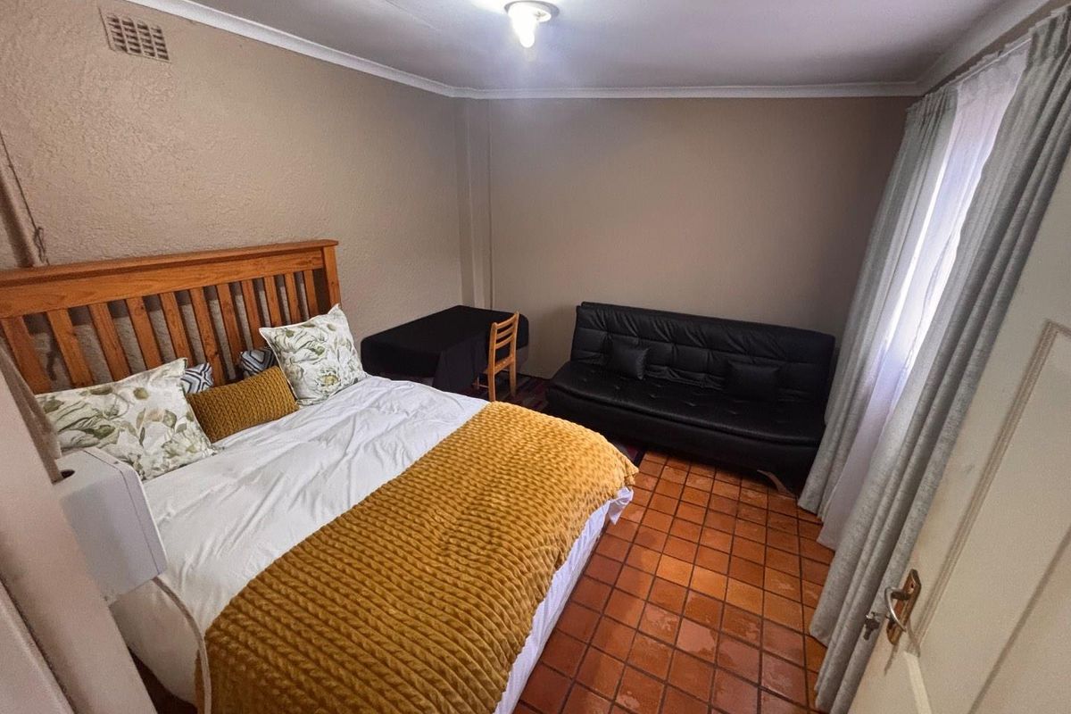 A bedroom featuring terracotta floor tiles, neutral wall paint, and a built-in ventilation vent.