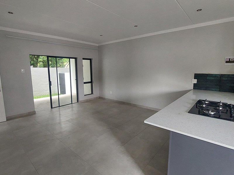 Modern open-plan living area featuring tiled floors, recessed lighting, and a kitchen island with a built-in gas hob, leading to an outdoor patio space.