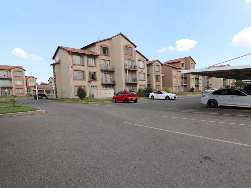 Exterior view of a multi-story apartment complex featuring paved parking areas, covered carports, and residential units with balconies.