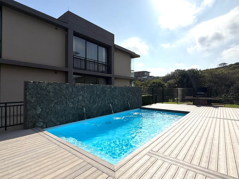 Outdoor pool area featuring a modern swimming pool with a stone water feature wall, timber decking, and a built-in braai area.