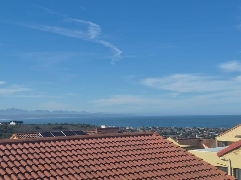 Elevated coastal view overlooking the surrounding neighborhood and ocean, featuring a terracotta tiled roof with integrated solar panels.