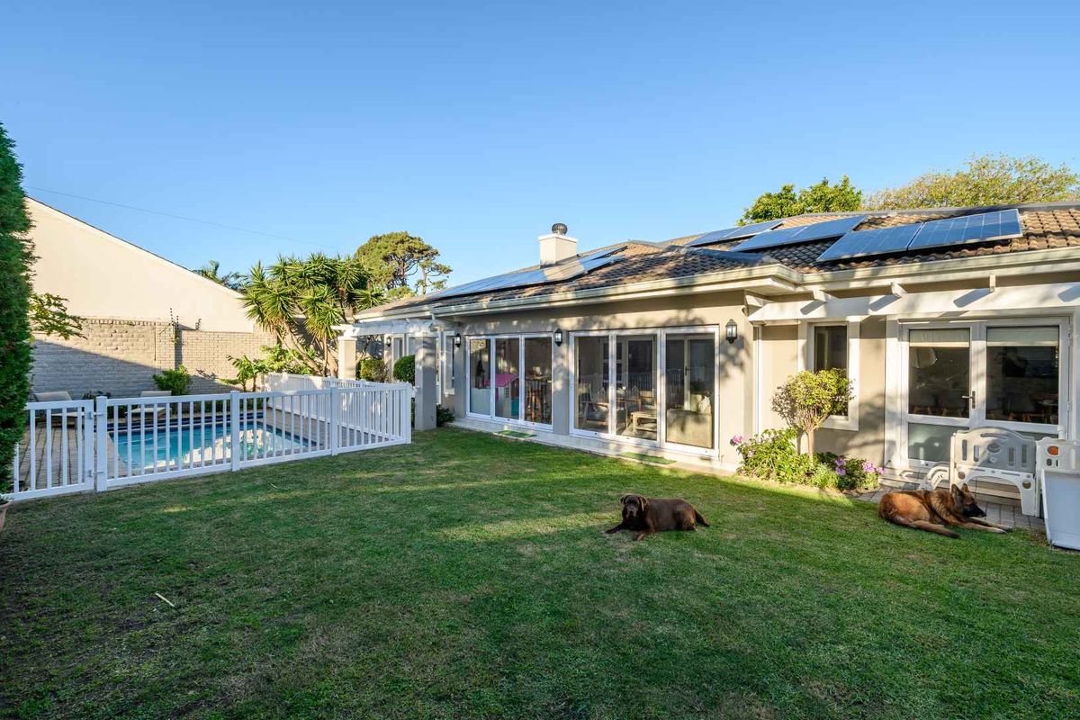 Rear view of the property featuring a landscaped garden, swimming pool with safety fencing, and solar panels installed on the tiled roof.