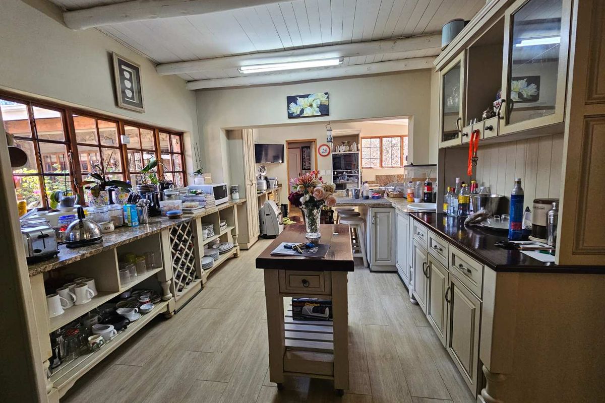 Spacious farmhouse-style kitchen featuring extensive built-in cabinetry, granite countertops, exposed beam ceilings, and large timber-framed windows overlooking the garden.