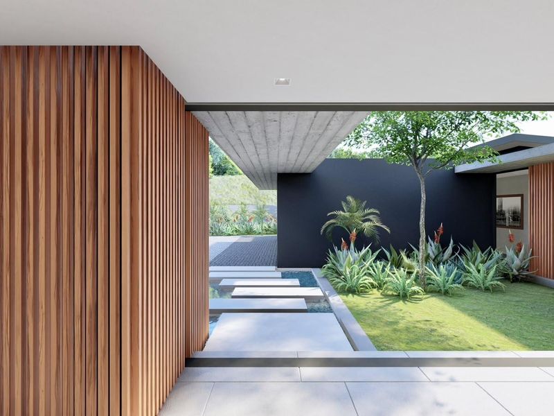 A modern covered patio area featuring timber slat wall cladding, an exposed concrete ceiling, and a serene garden with a water feature and stepping stones.